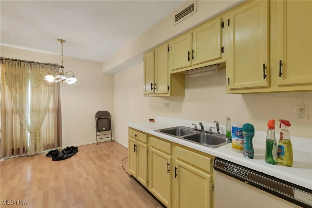 Kitchen featuring cream cabinetry, light countertops, dishwasher, pendant lighting, and light wood-style flooring