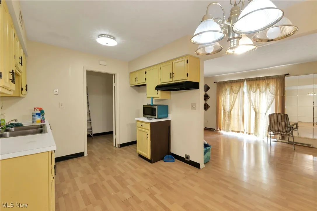 Kitchen with light countertops, light wood-type flooring, stainless steel microwave, under cabinet range hood, and a chandelier