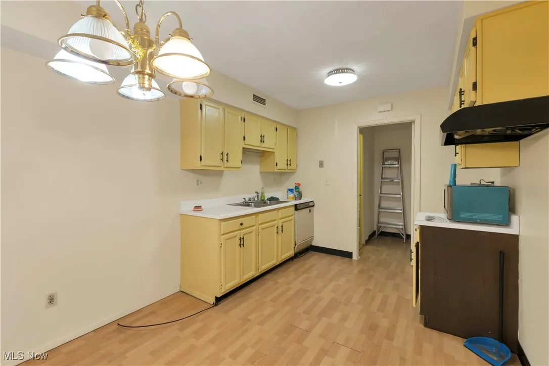 Kitchen featuring light countertops, pendant lighting, light wood-style flooring, under cabinet range hood, and a chandelier