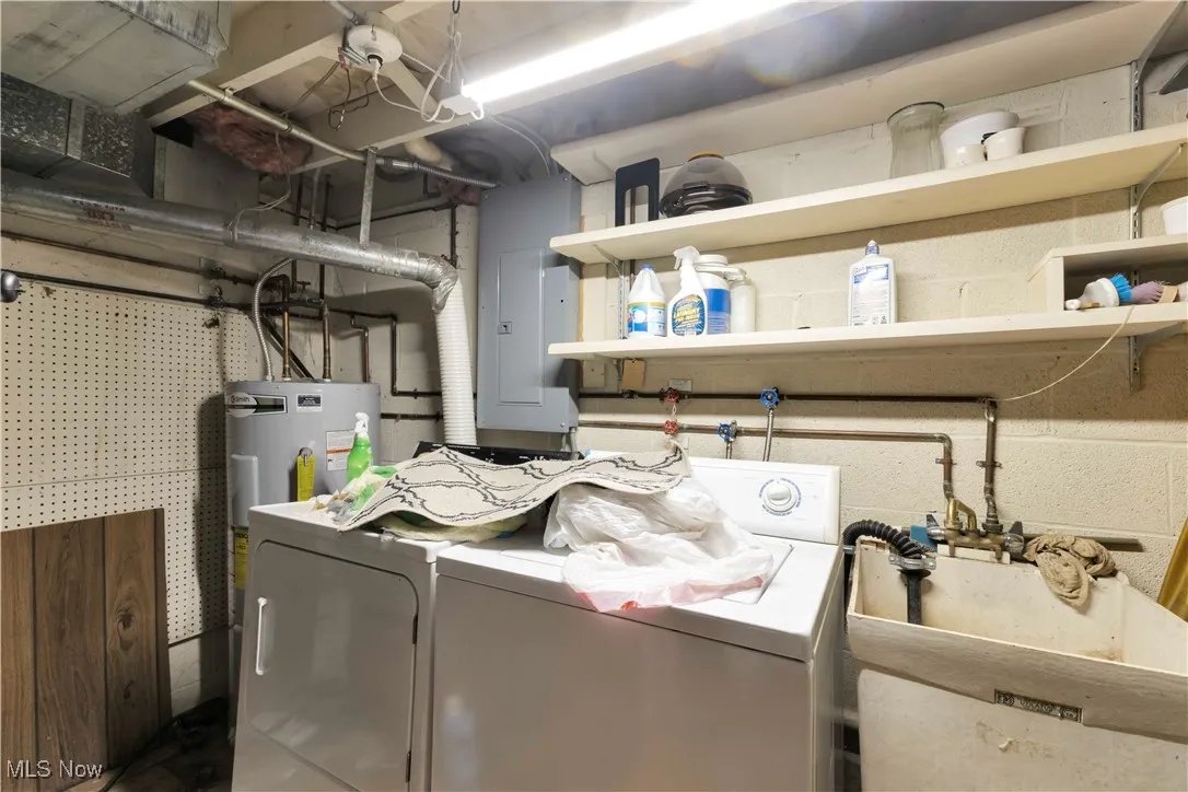 Washroom featuring electric panel, electric water heater, and washing machine and clothes dryer