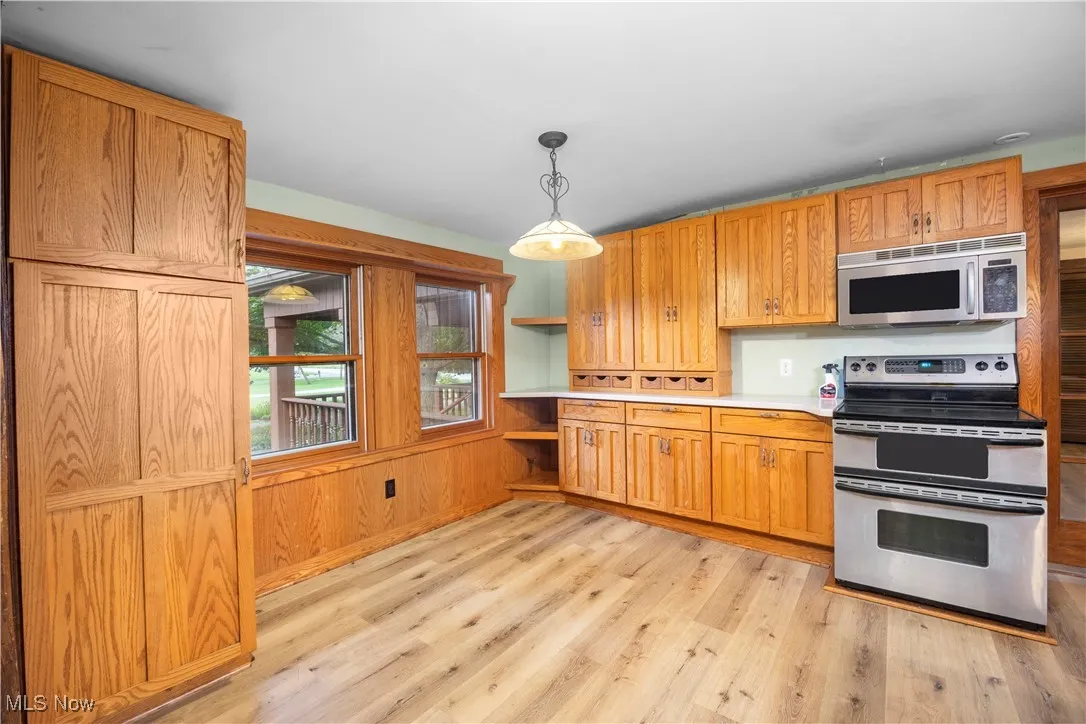Kitchen with stainless steel appliances, light countertops, hanging light fixtures, light wood-style flooring, and brown cabinets