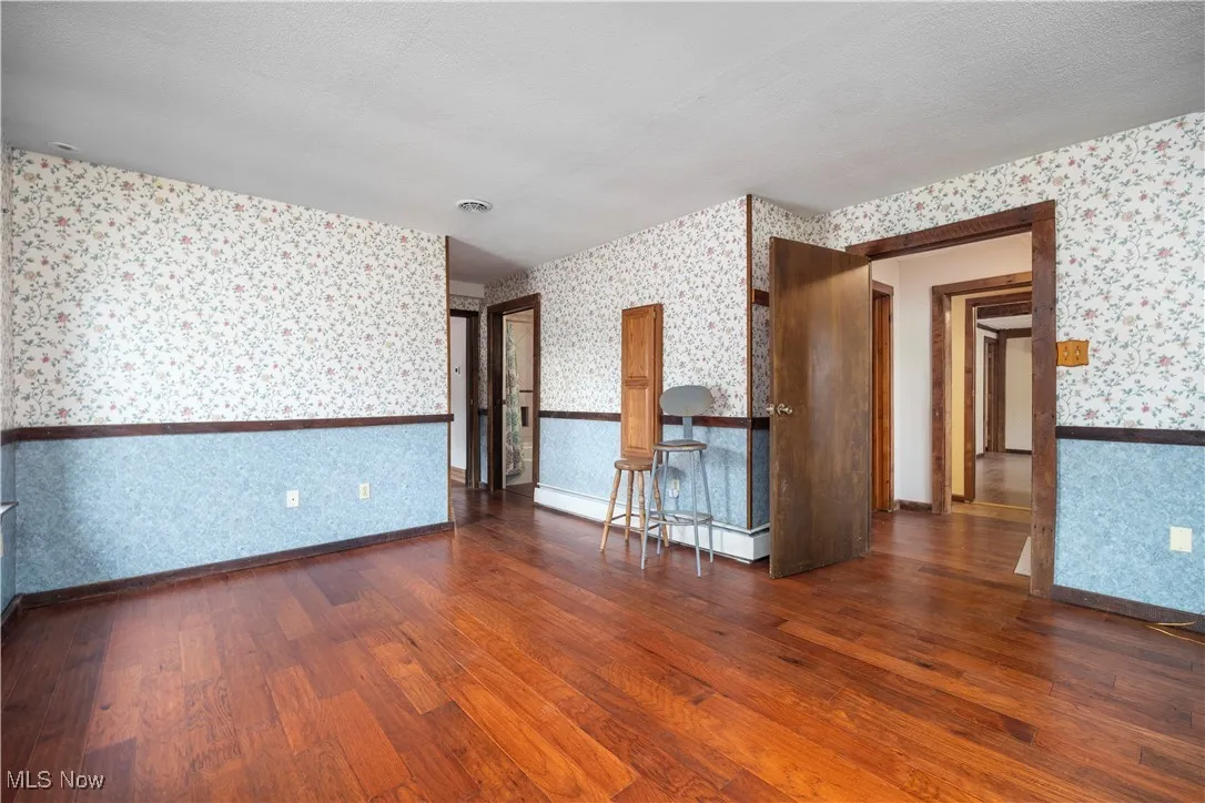 Unfurnished room featuring dark wood-style floors, wallpapered walls, and a textured ceiling