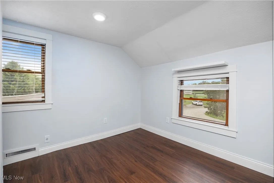 Spare room featuring dark wood-type flooring and lofted ceiling