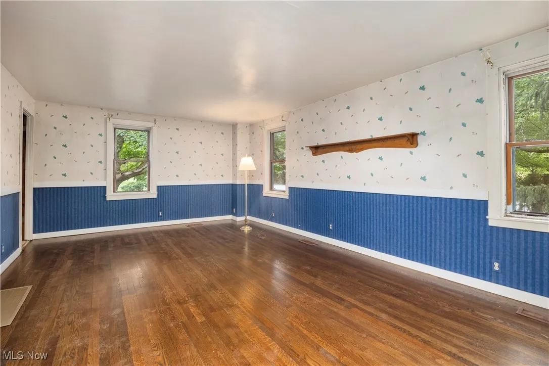 Unfurnished room with wallpapered walls, dark wood-style floors, and a wainscoted wall