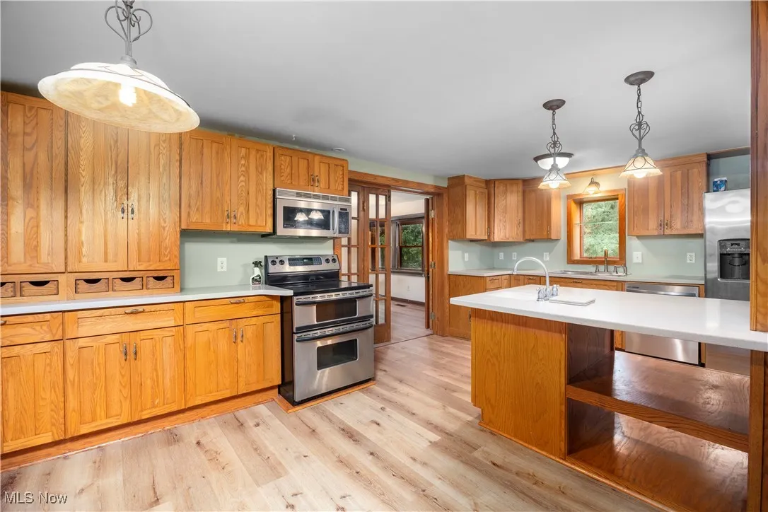 Kitchen with decorative light fixtures, stainless steel appliances, light countertops, and brown cabinets