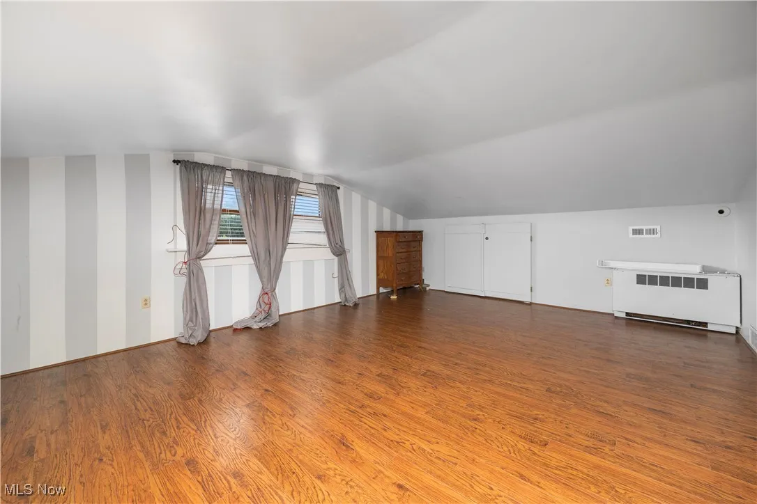 Additional living space with wood finished floors, radiator heating unit, and lofted ceiling