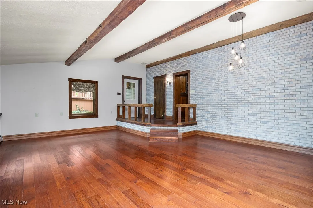Unfurnished room with wood-type flooring, brick wall, and beam ceiling