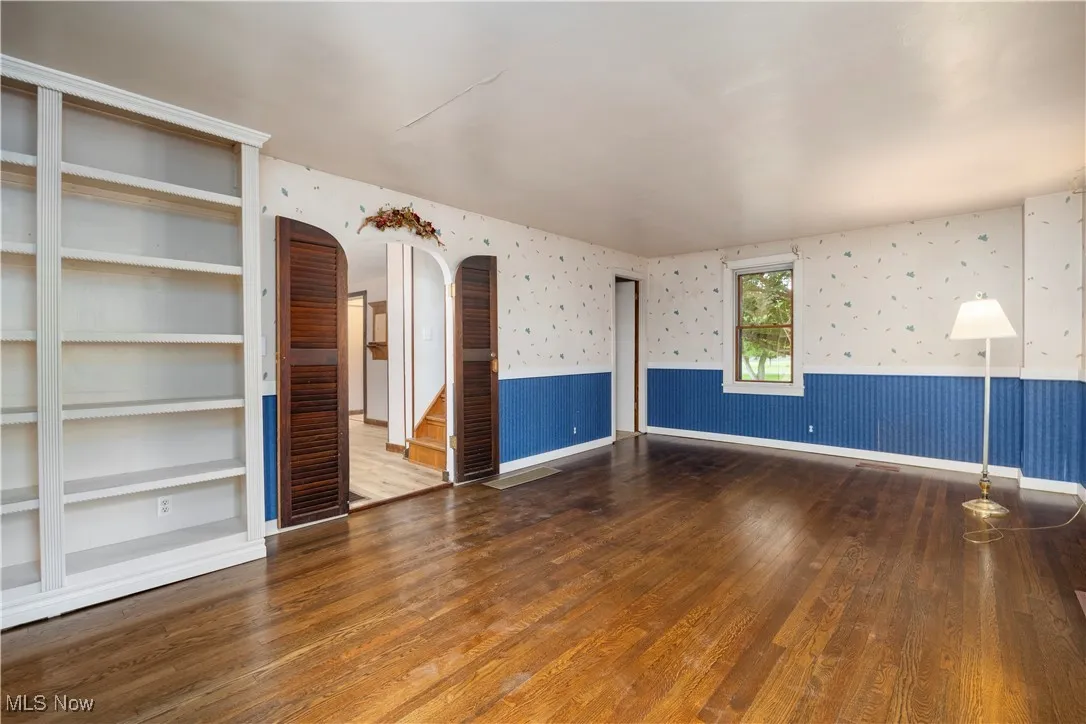 Unfurnished room featuring wallpapered walls, dark wood-type flooring, arched walkways, and wainscoting