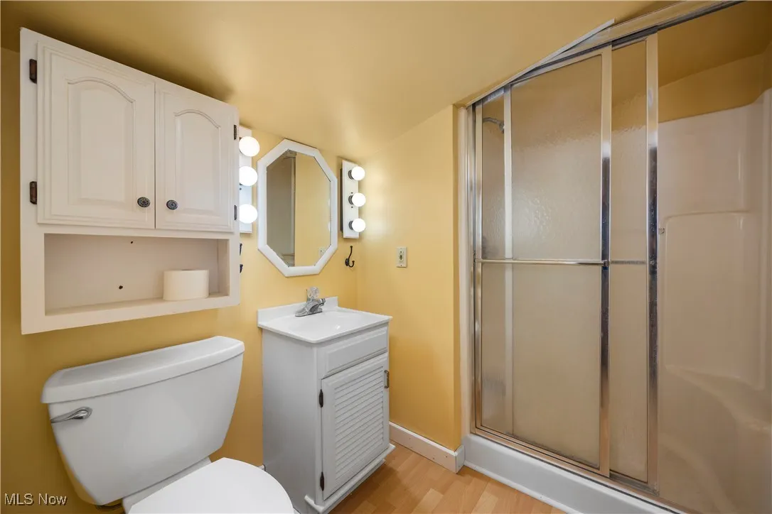 Full bath with vanity, a stall shower, light wood-style flooring, and lofted ceiling