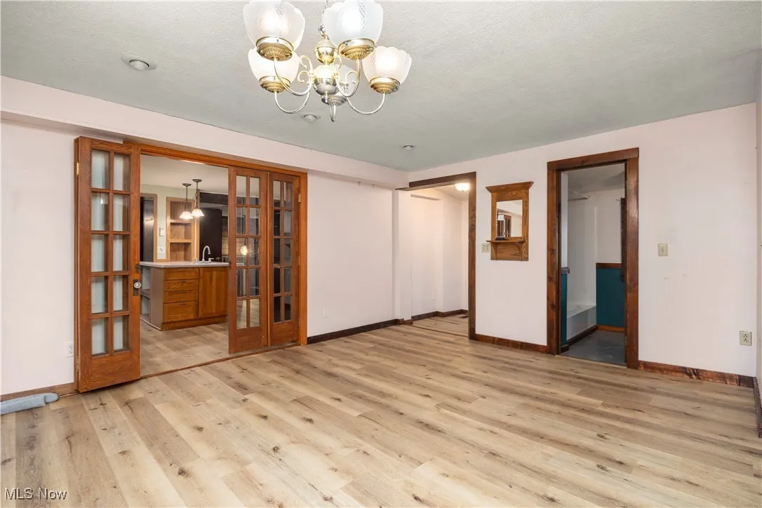 Unfurnished dining area with french doors, light wood finished floors, a chandelier, and a textured ceiling