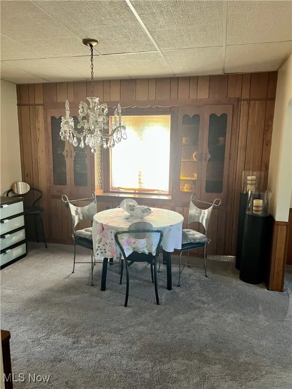 Carpeted dining area featuring wooden walls and a chandelier