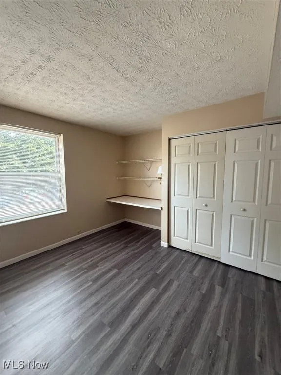 Unfurnished bedroom featuring dark wood-style floors, a textured ceiling, and a closet