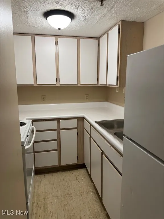 Kitchen featuring white cabinetry, fridge, light countertops, range, and a textured ceiling