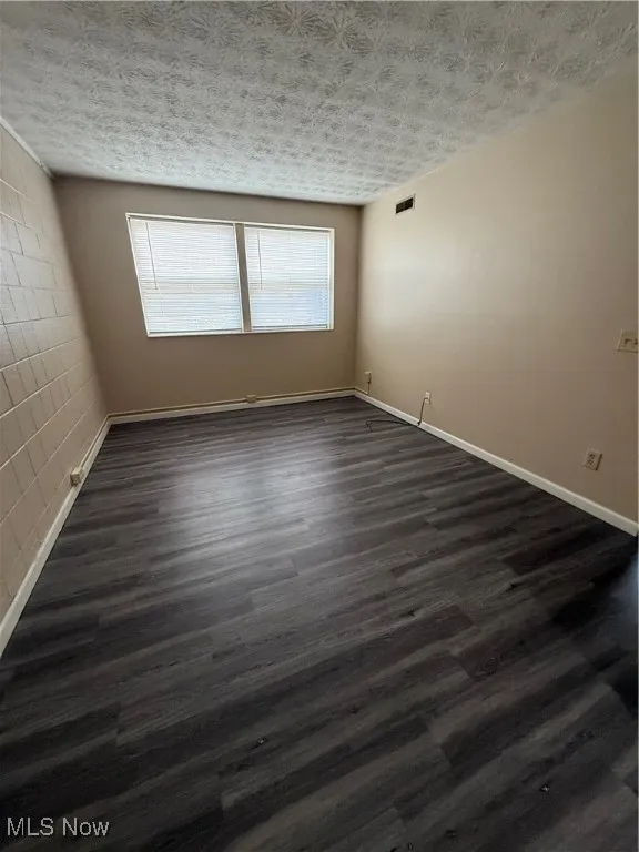 Unfurnished room featuring dark wood-style flooring and baseboards