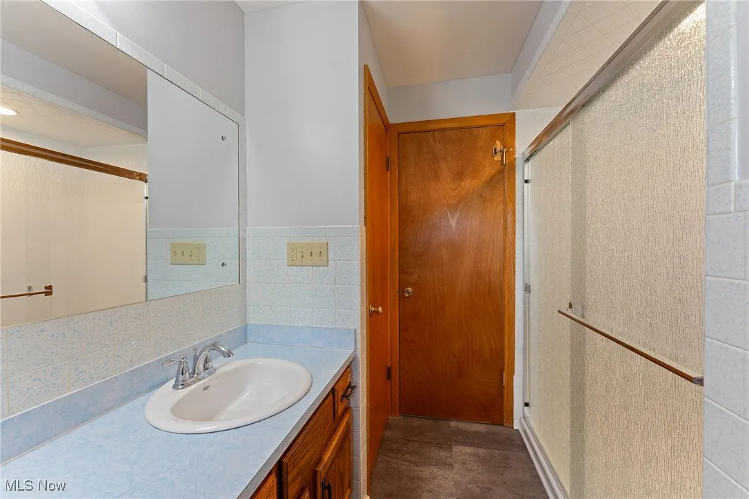 Full bath featuring a stall shower, vanity, and tile walls