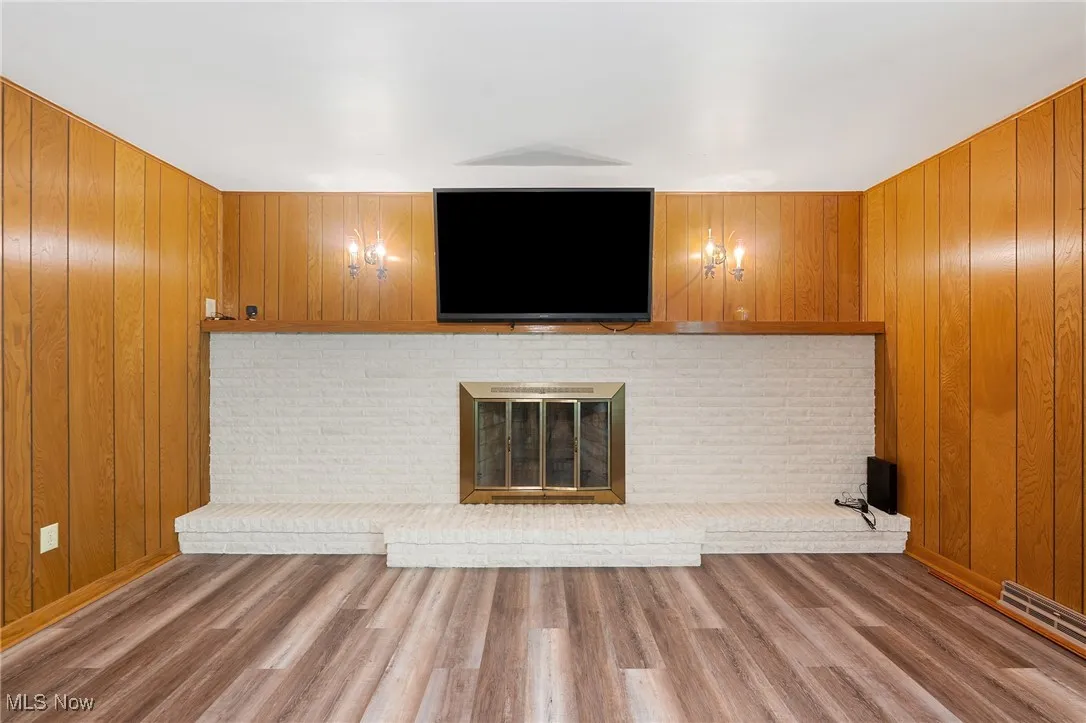 Unfurnished living room featuring wooden walls, wood finished floors, and a fireplace