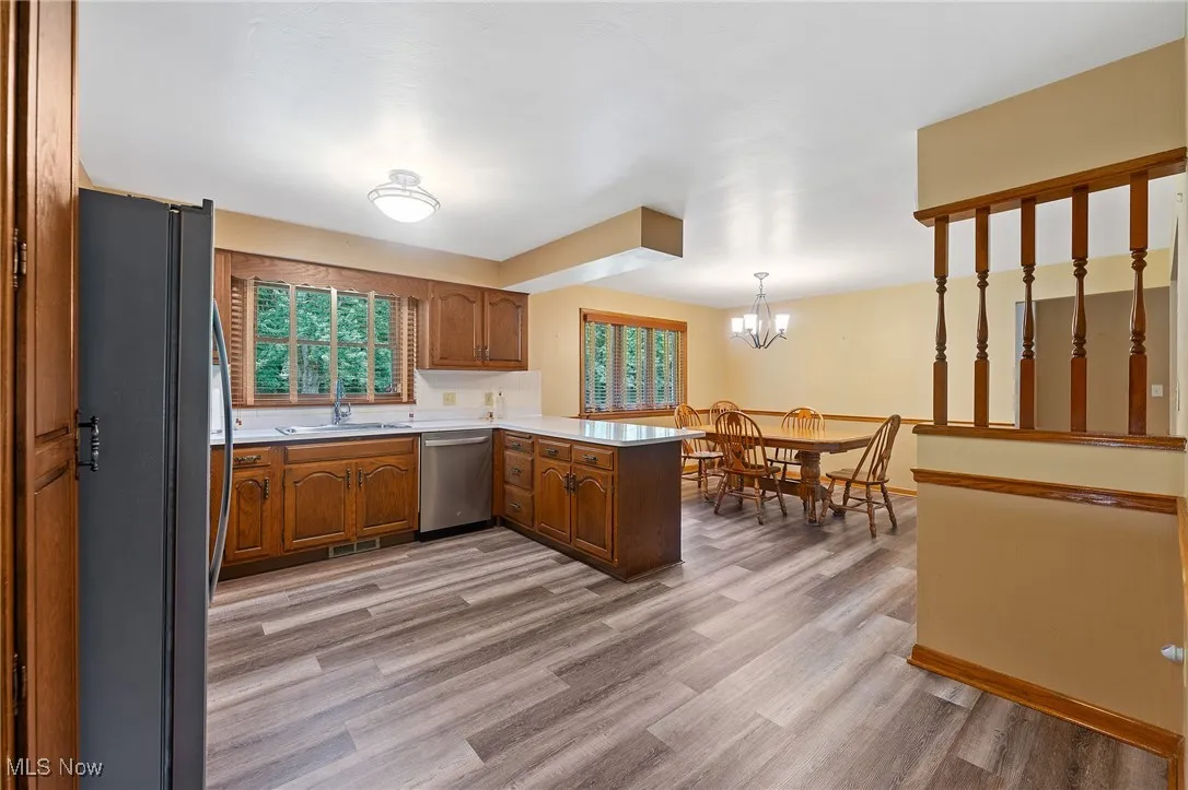 Kitchen with brown cabinetry, light countertops, freestanding refrigerator, hanging light fixtures, and a peninsula