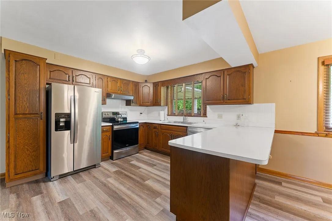 Kitchen featuring appliances with stainless steel finishes, a peninsula, brown cabinets, light countertops, and light wood finished floors