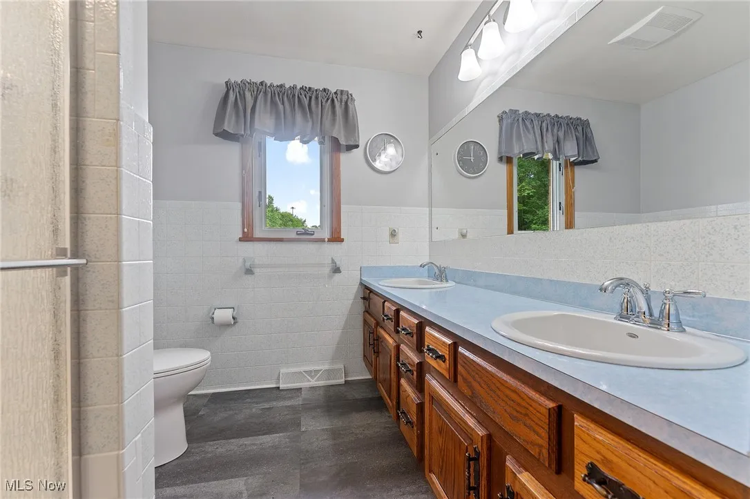 Full bath featuring a wainscoted wall, tile walls, double vanity, and a shower with shower door