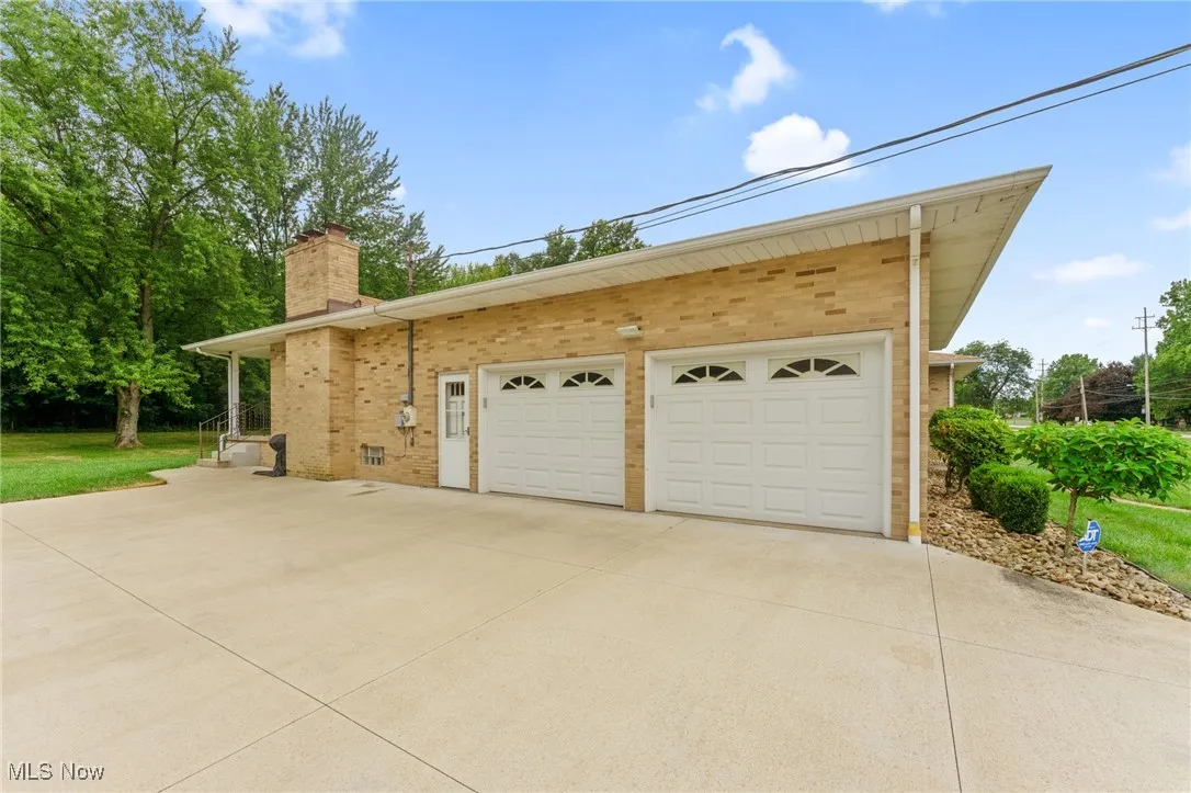 View of home's exterior featuring a chimney, brick siding, driveway, and an attached garage