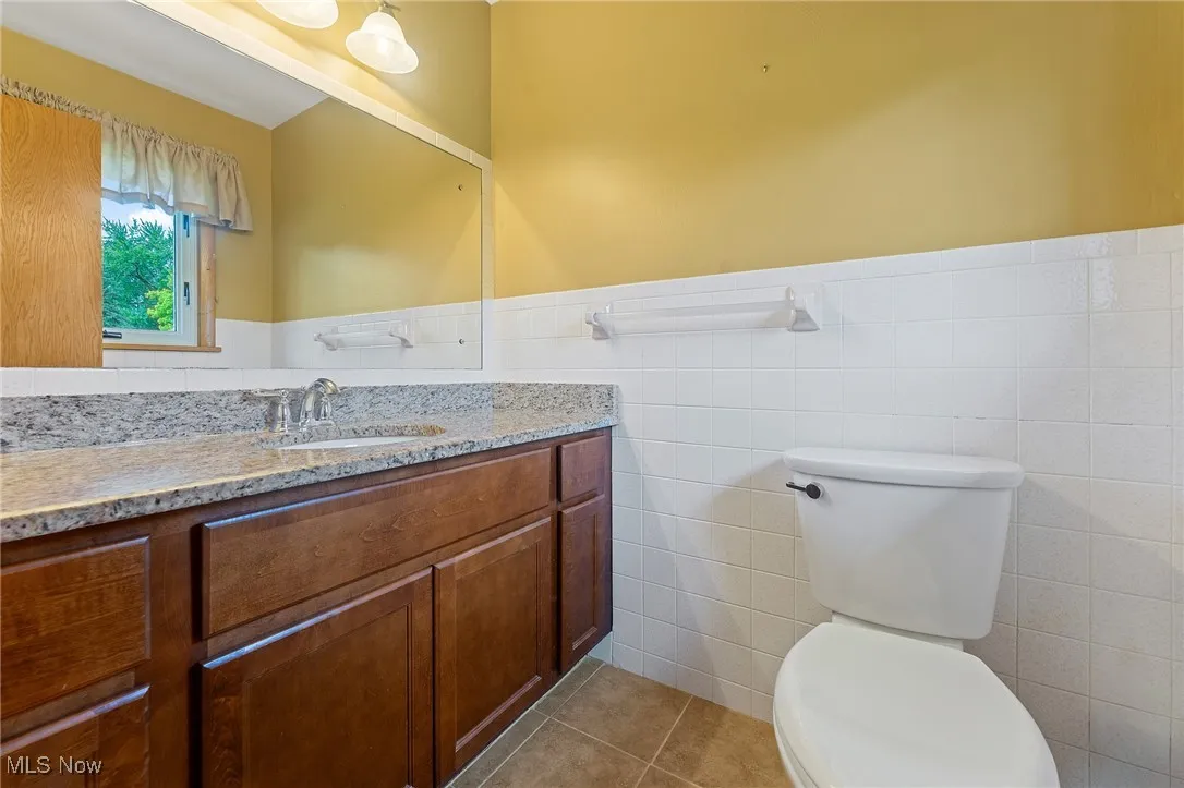 Master en suite half bath featuring light tile patterned floors, vanity, tile walls, and wainscoting