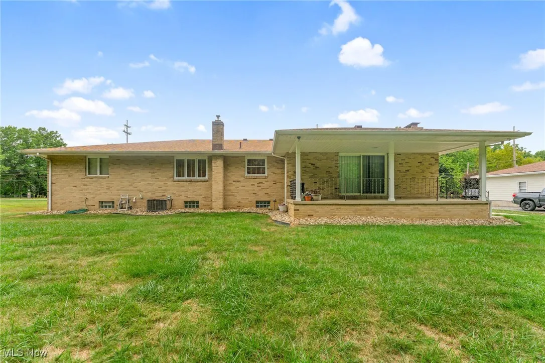 Back of house with brick siding, a lawn, a chimney, and a patio area