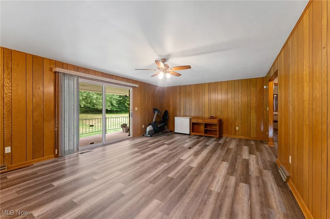 Unfurnished living room featuring wood walls, wood finished floors, and ceiling fan