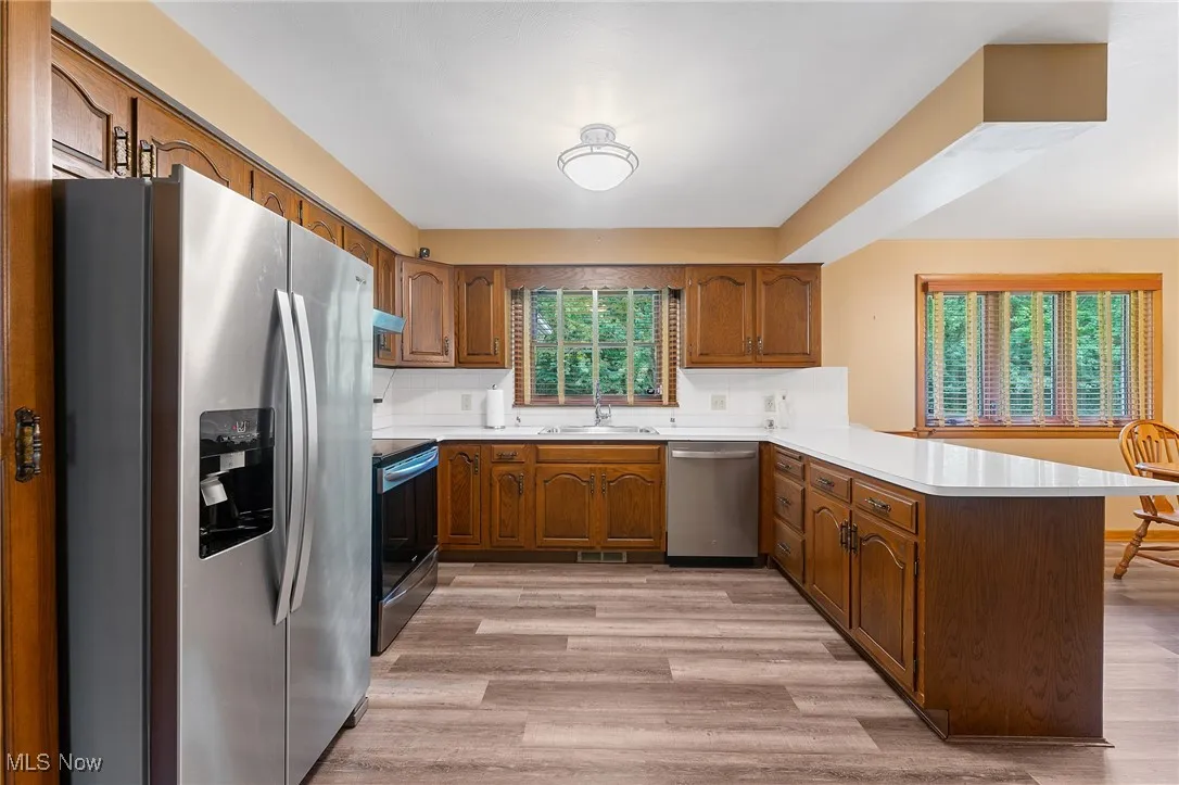 Kitchen with stainless steel appliances, a peninsula, brown cabinetry, light countertops, and light wood-style floors