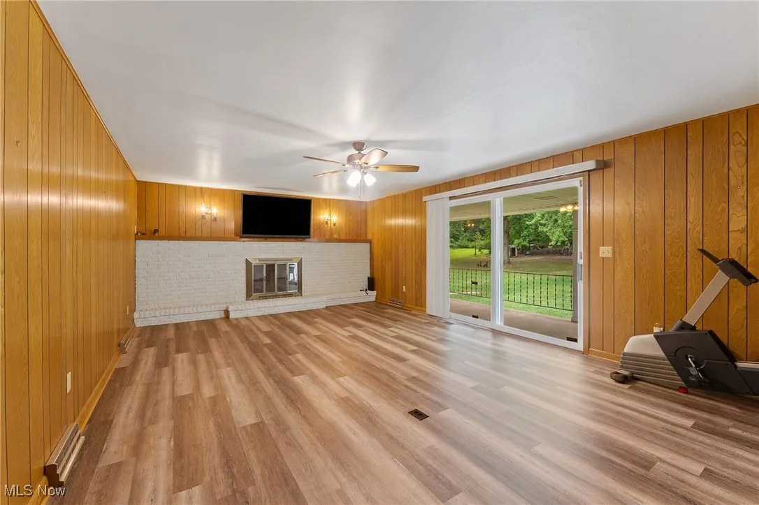 Unfurnished living room featuring wooden walls, a brick fireplace, a ceiling fan, and light wood-type flooring