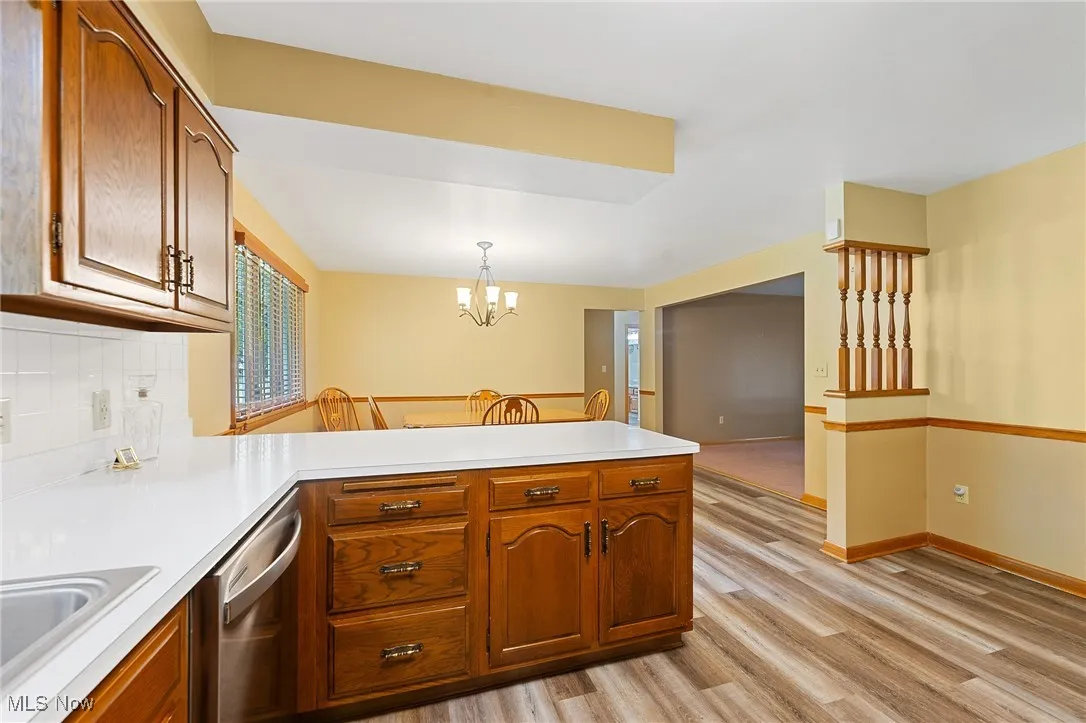 Kitchen featuring a peninsula, light countertops, light wood-style floors, tasteful backsplash, and a chandelier