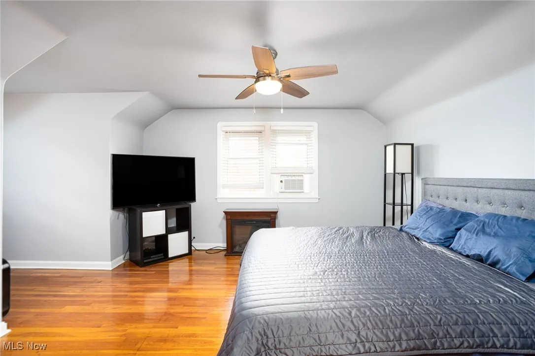 Bedroom featuring wood finished floors, vaulted ceiling, a ceiling fan, and cooling unit