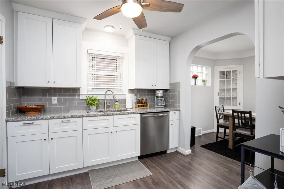 Kitchen with light stone counters, white cabinets, dishwasher, and arched walkways