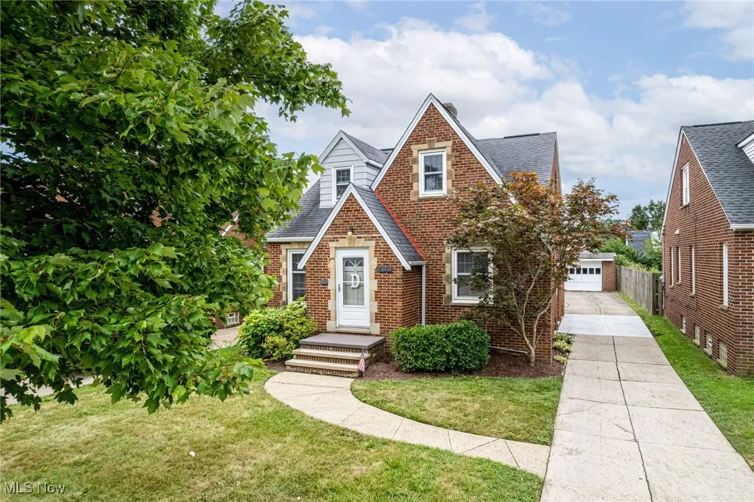 Tudor-style house with a shingled roof, a front yard, brick siding, and a garage