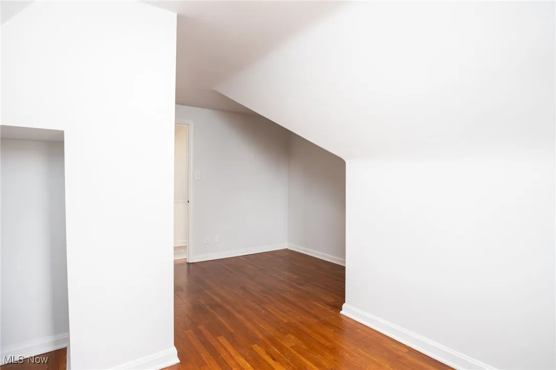 Additional living space with dark wood-type flooring and vaulted ceiling