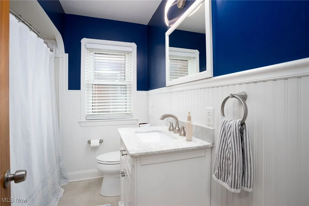 Full bathroom featuring wainscoting, vanity, a shower with shower curtain, and light tile patterned flooring