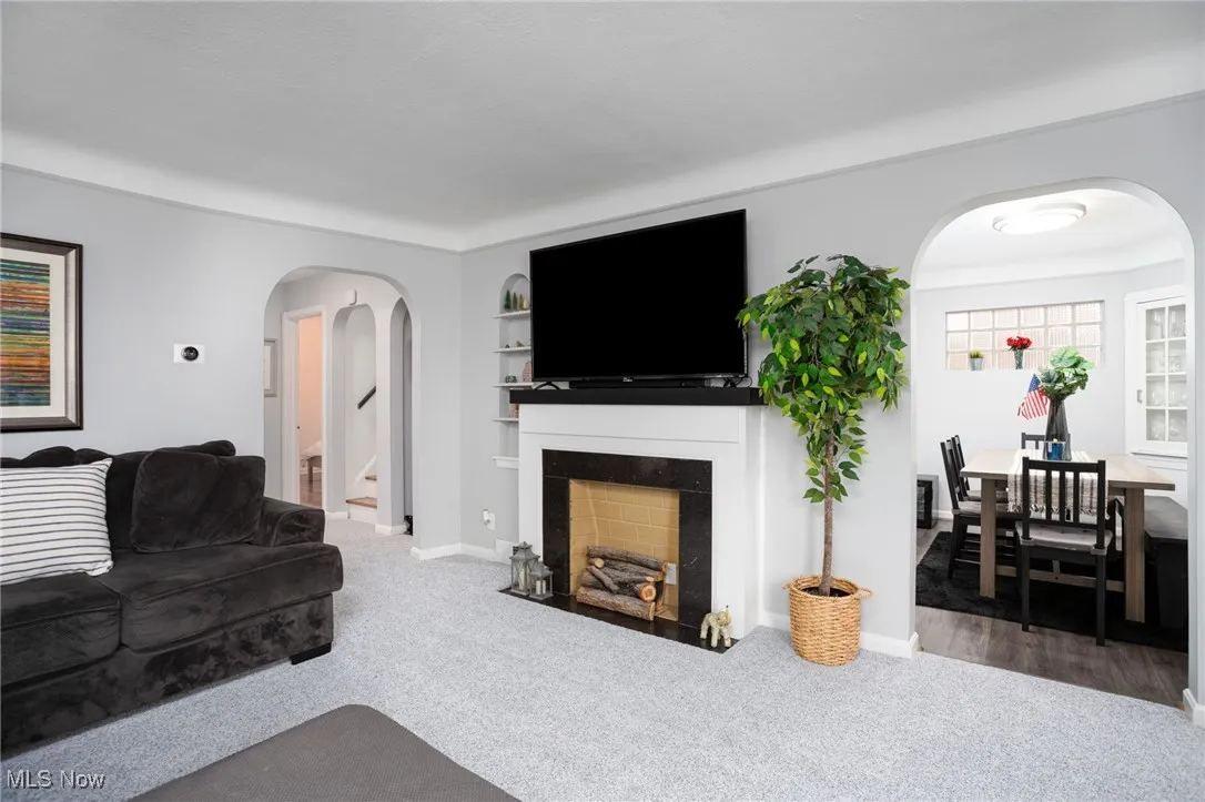 Carpeted living area featuring arched walkways, a fireplace with flush hearth, and built in shelves