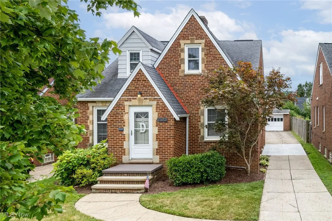 Tudor home featuring roof with shingles, brick siding, an outdoor structure, and a garage