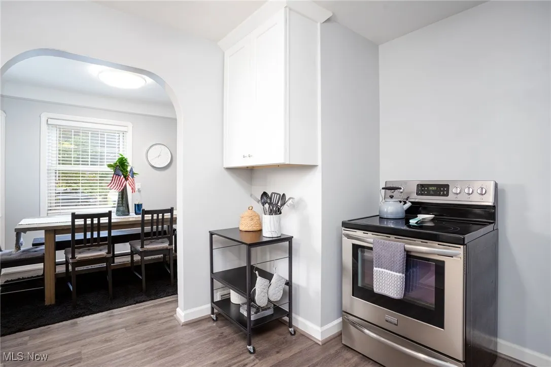 Kitchen featuring stainless steel range with electric stovetop, arched walkways, white cabinetry, and light hardwood floors
