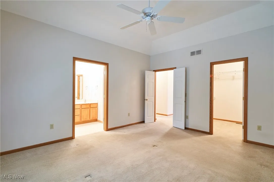 Master bedroom featuring a spacious closet, light carpet, a ceiling fan, and ensuite bath