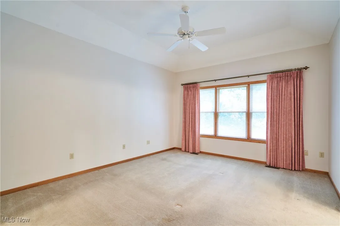 Master bedroom featuring light colored carpet, a tray ceiling, and ceiling fan