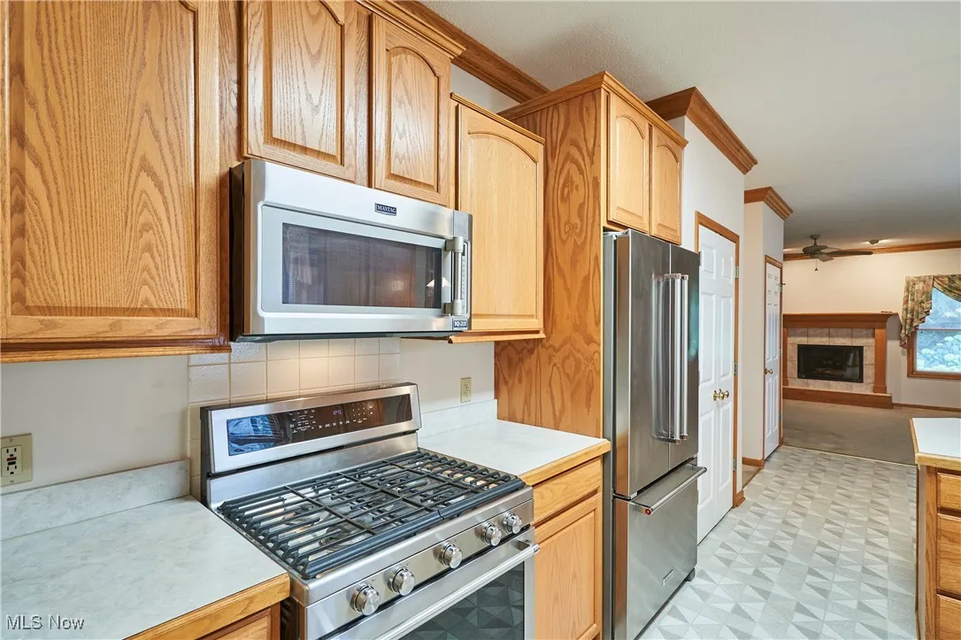 Kitchen with oak cabinets, appliances with stainless steel finishes, crown molding, and a  backsplash.