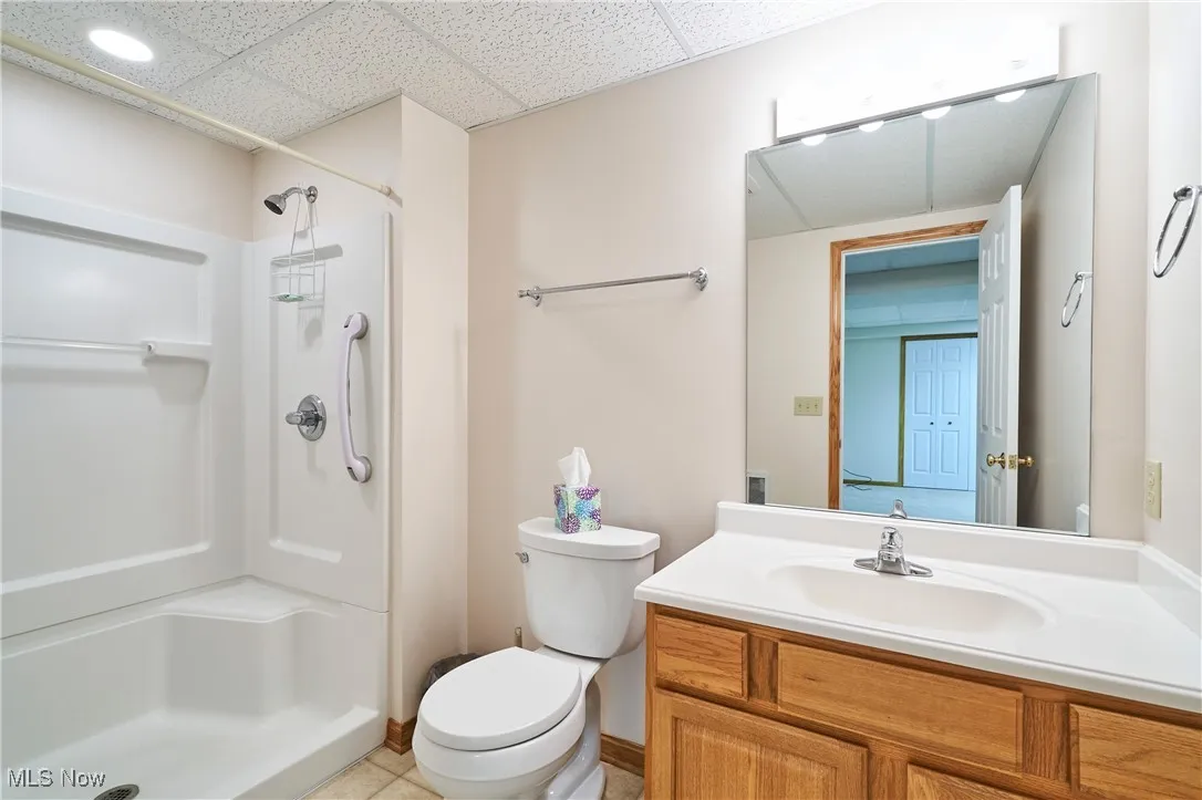 Full bath with vanity, a shower stall, a paneled ceiling located in the lower level