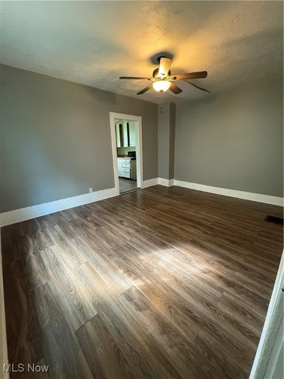 Spare room with a textured ceiling, dark wood-style flooring, and a ceiling fan