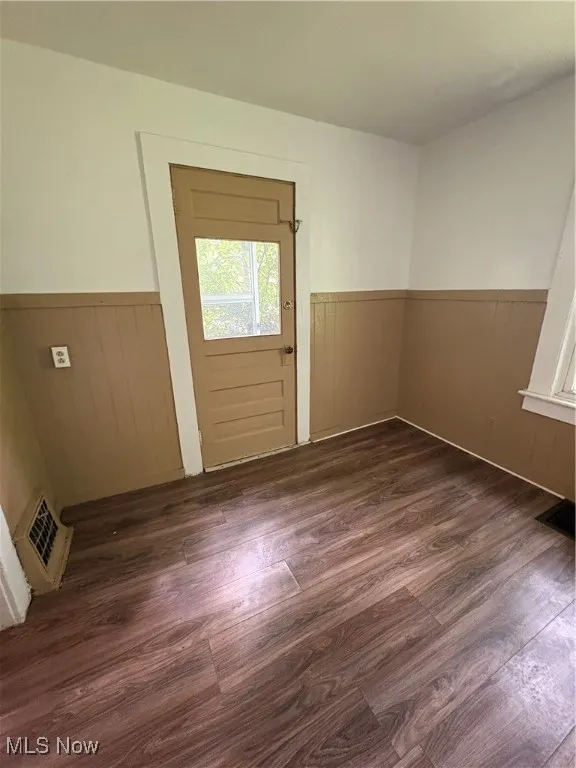 Empty room with a wainscoted wall, dark wood-style floors, and wooden walls