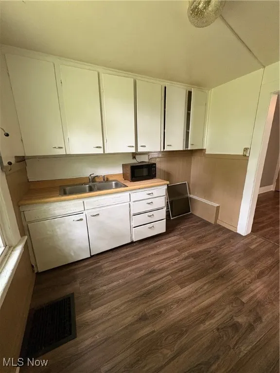 Kitchen with white cabinetry, light countertops, dark wood-style floors, and black microwave