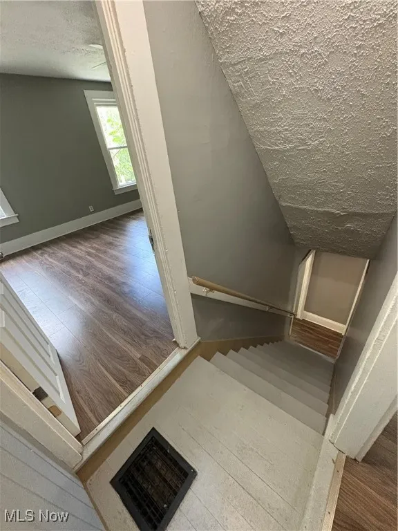 Stairs with a textured ceiling and wood finished floors