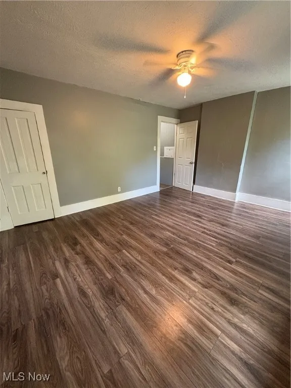 Unfurnished bedroom with a textured ceiling, dark wood-style floors, and ceiling fan