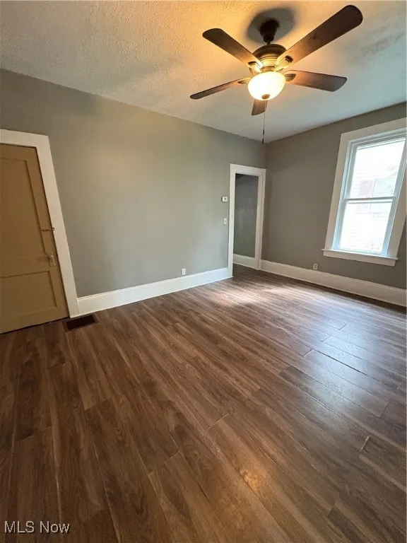 Spare room featuring dark wood-style flooring, a textured ceiling, and ceiling fan