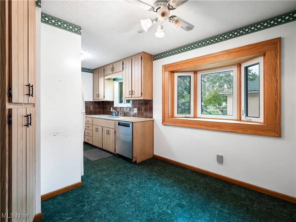 Kitchen featuring light countertops, backsplash, stainless steel dishwasher, a textured ceiling, and light brown cabinets