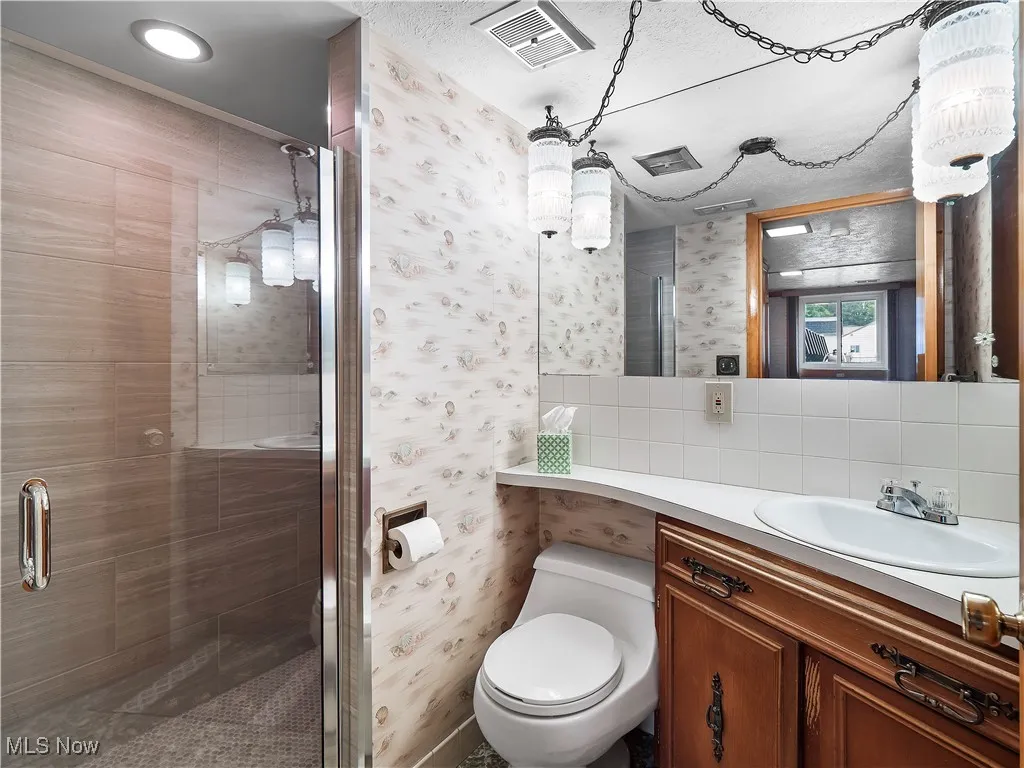 Full bathroom featuring wallpapered walls, a stall shower, vanity, and decorative backsplash